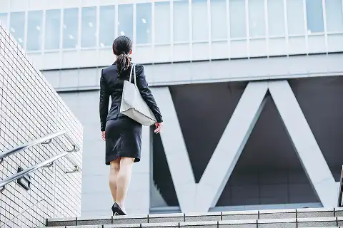 オフィスビルへ向かって階段を上るスーツ姿のビジネスパーソンの後ろ姿